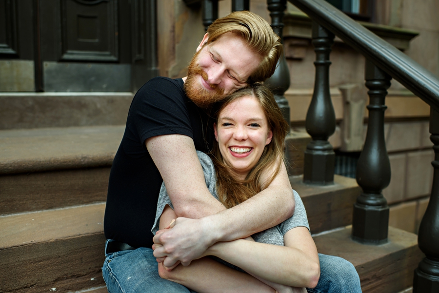 A laughing couple hug on the steps of a philly apartment during their engagement session.